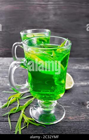 Limonade à l'estragon avec des brins d'estragon, des tranches de glace et de chaux dans deux gobelets sur fond de planche en bois noir Banque D'Images