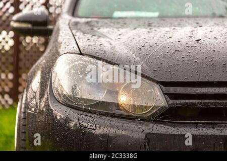 Voiture abaissée à réglage noir, debout sur l'herbe sous la pluie. Gros plan des phares, de la calandre, du pare-chocs avant. Banque D'Images