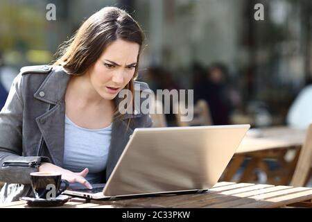 Une femme en colère appuie sur un bouton désespérée vérifier l'ordinateur portable dans une terrasse de café Banque D'Images