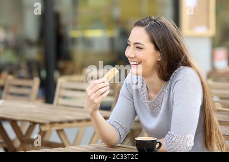 Heureuse jeune femme tenant un snack-bar à céréales assis sur une terrasse de café Banque D'Images