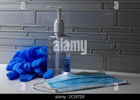 une bouteille de désinfectant pour les mains avec d'autres fournitures médicales, y compris des gants en caoutchouc et un masque facial sur un comptoir de cuisine devant un dosseret de carreaux Banque D'Images