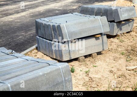 De larges et longues briques de béton neuves pour bordures de trottoir, se trouvant sur le sol du chantier de construction lors de la construction d'une nouvelle route Banque D'Images