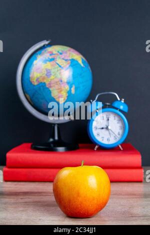 Le globe et l'horloge bleue se tiennent sur une pile de livres, à côté d'une pomme. Banque D'Images