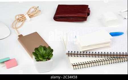 carnets, stylo, pile de cartes de visite, portefeuille en cuir marron et banque d'alimentation avec cordon sur une table blanche, lieu de travail Banque D'Images