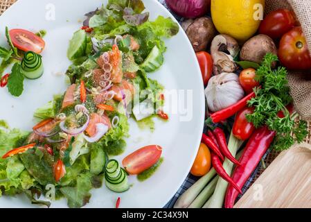 Salade de saumon frais avec légumes, salade saine avec feuilles de laitue mélangées sur un plat blanc sur une table rustique ancienne, recette facile, vue de dessus style thaïlandais Banque D'Images