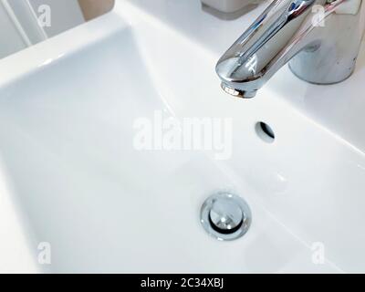 Robinet chromé avec levier pour mélanger l'eau chaude et froide sur un lavabo blanc moderne dans une salle de bains. Vie domestique et hygiène Banque D'Images