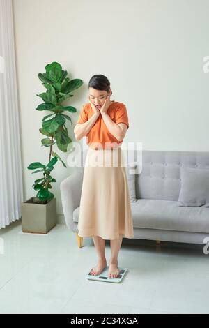 Belle jeune femme vérifiant son poids sur une simple balance blanche. Banque D'Images