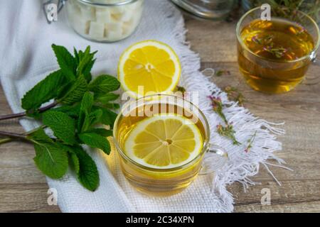 Tasse en verre transparent avec thé à la menthe sur un support en bois, à côté d'un bol à sucre avec des cubes de sucre, des tranches de citron et de feuilles de menthe. Banque D'Images