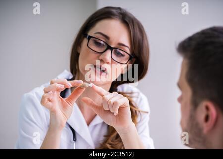 Jeune femme médecin montrant à l'aide auditive Male Patient In Clinic Banque D'Images