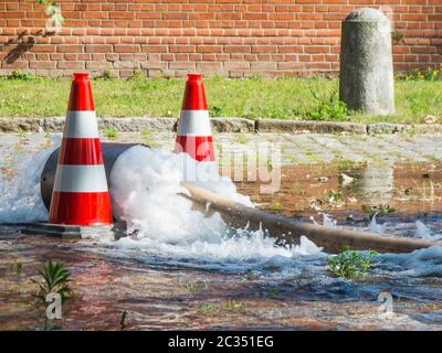 D'un tuyau d'incendie avec clapet anti-retour bouillant sur la rue de l'eau courante maintenue par deux rouges et blanc rayé Lübeck Cap (pylons) sur des pavés. Banque D'Images