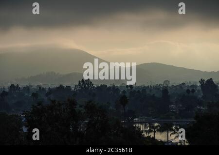 Belle vue tôt le matin du lac San Marcos, Californie avant les remontées de la couche marine, avec des montagnes, des nuages, des arbres, et le lac reflétant le ciel. Banque D'Images