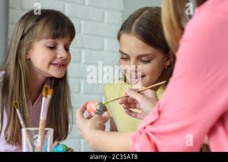 Les enfants regardent maman peindre les œufs de Pâques magnifiquement Banque D'Images