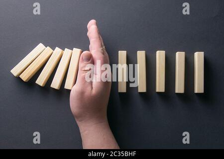 Vue de dessus homme de main arrêtant des dominos tombant dans une image conceptuelle de gestion de crise d'entreprise. Banque D'Images