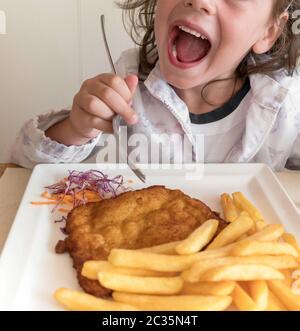 Peu d'Italien girl eating viande panées et frites Banque D'Images