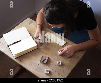 Femme gemmologiste travaillant à observer des pierres précieuses dans son espace de travail. Table en bois avec carnet, daim, pelle et pierres précieuses Banque D'Images