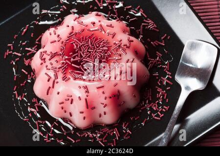 Dessert au lait rose aux saveurs de framboise ou de fraise servi sur une assiette noire. Banque D'Images