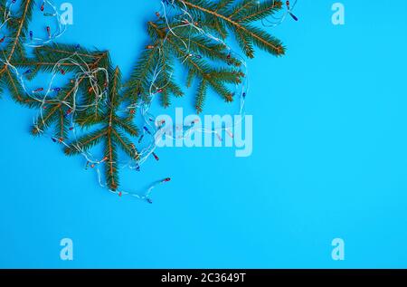 Burning ampoules colorées sur une guirlande avec un câble blanc et vert les brindilles d'aiguilles, fond bleu, copy space Banque D'Images
