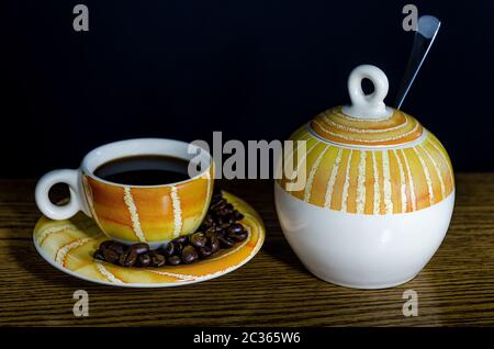 Tasse à café jaune et orange et bol à sucre sur une table, avec grains de café et fond noir Banque D'Images