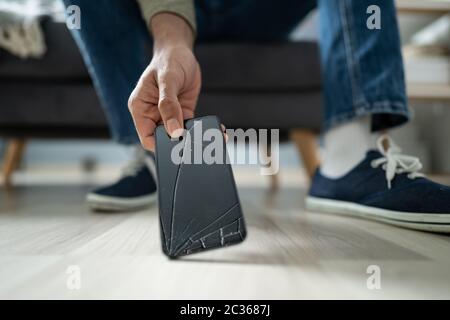 Close-up of a Man Picking Up The Broken Smart Phone de plancher de bois franc Banque D'Images