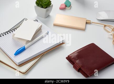 carnets, stylo, pile de cartes de visite, portefeuille en cuir marron et banque d'alimentation avec cordon sur une table blanche, lieu de travail, vue de dessus Banque D'Images