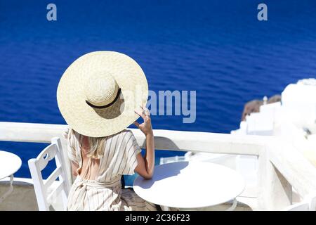 Jeune femme vêtue d'une robe blanche et chapeau de paille, marchant dans la ville d'Oia, île de Santorini, Grèce Banque D'Images