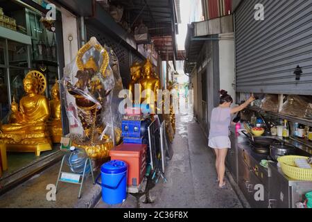 Dans une ruelle au large de Bamrung Muang Road, Bangkok, Thaïlande, une femme exploite une cabine de nourriture à côté d'un magasin vendant des statues de Bouddha et d'autres objets de dévotion Banque D'Images