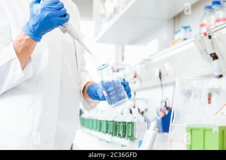 Gros plan d'une main de médecins portant des gants bleus en utilisant un compte-gouttes pour pendre l'échantillon du flacon Banque D'Images