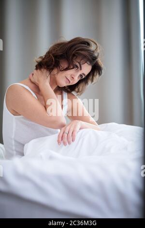 Jolie jeune femme avec une raideur de la nuque, maux de dos, dans son lit le matin Banque D'Images