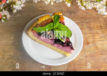 Des tranches de mousse de myrtilles avec des baies décorées de verglas miroir et des feuilles de menthe sur une plaque blanche avec des fleurs blanches sont sur table en bois, à proximité Banque D'Images