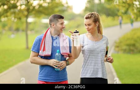 Jeune couple courant et bavardant dans le parc de la ville. Joyeux caucasien moderne homme et femme dans les casques jogging dans la nature et vivre en bonne santé à l'extérieur Banque D'Images