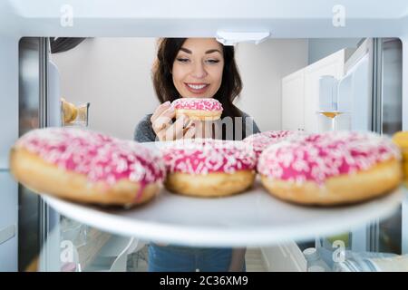 Bonne jeune femme prenant le Donut du réfrigérateur ou du congélateur Banque D'Images