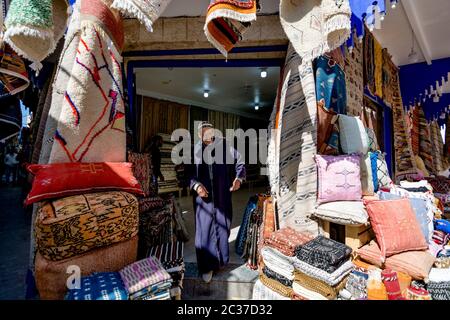 Essaouira, Maroc, février 2019: Vendeur de textiles, tapis et tapis artisanaux marocains au marché de rue. Médina marocaine avec boutiques Banque D'Images