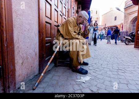 Marrakech, Maroc, février 2019 : vieil homme pauvre musulman avec un bâton de marche au marché traditionnel de rue au Maroc. Médina marocaine avec souk, boutique Banque D'Images