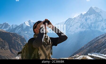 Randonneur regardant à travers des jumelles sur un sentier de randonnée au camp de base d'Annapurna, l'Himalaya, Népal. Paysage de montagne de l'Himalaya dans l'Annapurna r Banque D'Images