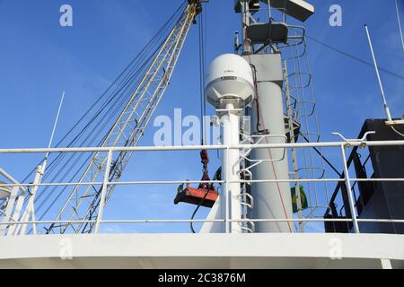 Antenne satellite avec mât radar du navire marchand avec la grue de chargement en arrière-plan pendant les opérations de fret lorsque le navire est dans le port Banque D'Images