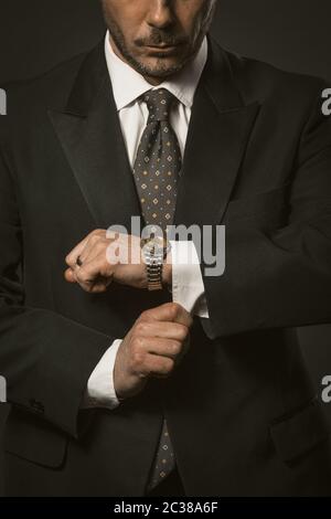 L'homme d'affaires vérifie le temps. Bien habillé de cols blancs, le barbu caucasien regarde la montre-bracelet qui règle les poignets de chemise. Gros plan. Teinté Banque D'Images