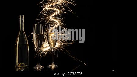 Des verres et une bouteille de champagne dans les lumières du Bengale. Arrière-plan noir. Concept de célébration et nouvel an. Banque D'Images