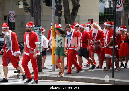 Les personnes vêtues du Père Noël prenant part au SantaCon de Sydney traversent la rue Crown Street à Surry Hills. Banque D'Images