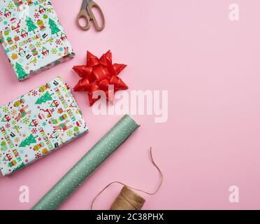 Avec les rouleaux de papier d'emballage, brown rope, ciseaux, et un décor boîte carrée enveloppée avec un cadeau. Cadeaux bricolage décisions, sur fond rose Banque D'Images
