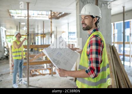 Chantier. Travailleur du bâtiment dans le plan de maintien de gilet jaune, son collègue debout dans l'arrière-plan, en vérifiant la construction Banque D'Images