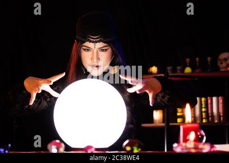 Une femme noire habillée de sorcière exécute un rituel dans une pièce mystérieuse, horrifiante et abrupte. Crystal ball brille. Banque D'Images