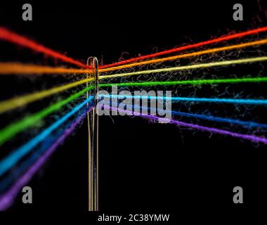 Les fils multicolores, formant les couleurs de l'arc-en-ciel, sont filés à travers l'œil d'une aiguille à coudre, macro Banque D'Images