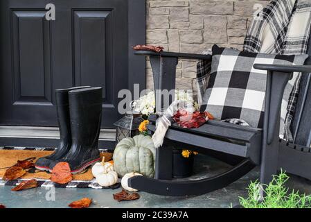 Véranda traditionnelle décorée pour l'automne avec bottes de pluie, gourdes de bruyère, citrouilles blanches, mamans et chaise à bascule avec coussin à carreaux de buffle Banque D'Images