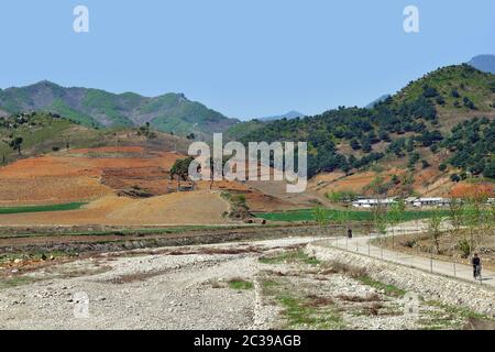 Région de Wondan, Corée du Nord - 3 mai 2019 : route de terre et champs agricoles. Un homme local fait des promenades à vélo. Paysage nord-coréen Banque D'Images