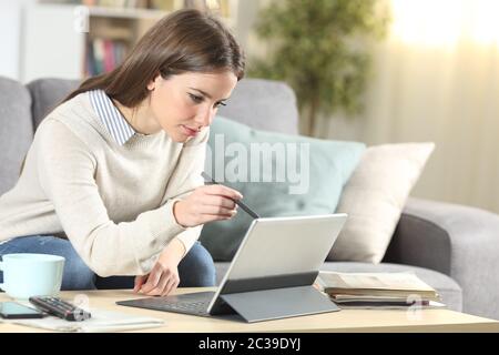 Femme à l'aide de stylo tactile sur tablet assis sur un canapé dans la salle de séjour à la maison Banque D'Images