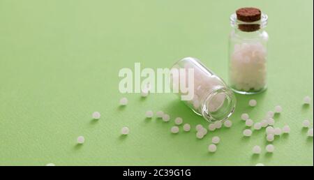 Homéopathie, globules dispersés dans une bouteille de verre, fond vert. Médecine alternative naturelle, espace de copie Banque D'Images