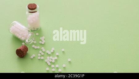 Homéopathie, globules dispersés dans une bouteille de verre, fond vert. Médecine alternative naturelle, espace de copie Banque D'Images