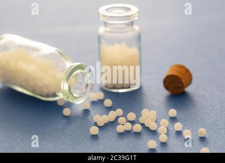 Homéopathie, globules dispersés dans une bouteille de verre, fond bleu. Médecine alternative naturelle, gros plan Banque D'Images