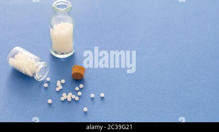 Homéopathie, globules dispersés dans une bouteille de verre, fond bleu. Médecine alternative naturelle, espace de copie Banque D'Images