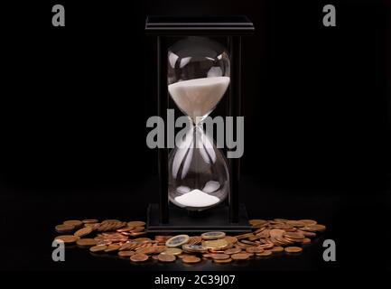 Time is money concept, les pièces en euros et hourglass sur fond noir. Studio shot. Banque D'Images